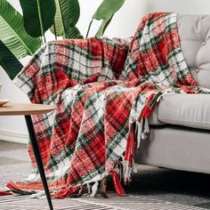 a red and green plaid blanket sitting on top of a couch next to a potted plant