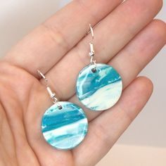 a pair of earrings with blue and white marbled designs on them, in the palm of someone's hand