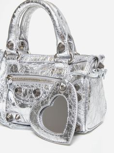 Balenciaga's Le Cagole Nano bag in Arena silver-tone metallic leather featuring double top handles, detachable shoulder strap, main compartment and front pocket closed by zip, detachable heart mirror charm and signature engraved silve-tone metal hardware. Composition: 100% lambskin Silver Designer Shoulder Bag With Detachable Strap, Luxury Silver Shoulder Bag With Detachable Strap, Designer Silver Top Handle Bag, Designer Silver Top Handle Shoulder Bag, Silver Handheld Shoulder Bag With Silver-tone Hardware, Designer Silver Bag With Detachable Strap, Designer Silver Bag With Detachable Handle, Silver Top Handle Shoulder Bag With Detachable Strap, Luxury Silver Shoulder Bag With Detachable Handle