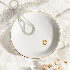 a white and gold plate with an e on the side, next to dried flowers