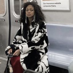 a woman is sitting on a train with her luggage in hand and looking off to the side