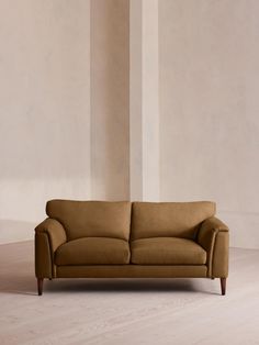 a brown couch sitting on top of a hard wood floor next to a white wall