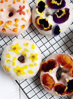 four donuts decorated with flowers and icing on a cooling rack