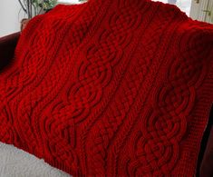 a red knitted blanket sitting on top of a couch next to a potted plant