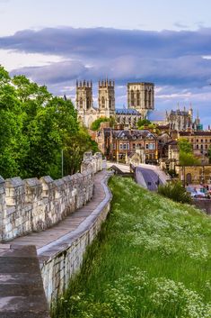 an old city with tall buildings and green grass on the hillside below it is a stone wall