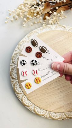 a person is holding up some earrings on top of a wooden tray with flowers in the background