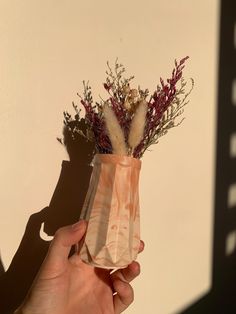 a person holding a vase with dried flowers in it on a white wall behind them