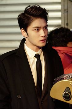 the young man is wearing a black suit and white shirt with a gold bell on his lapel