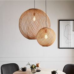 three lights hanging from the ceiling above a table with two chairs and a vase on it