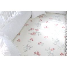 a white crib bed with pink flowers on the sheets and pillow cases next to it