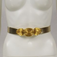 This pretty vintage belt is made of a 1-1/8" wide metallic gold band.  It does not say leather on the back, so it is probably faux leather.  The fancy front buckle is made of gold tone metal that has a concentric circle design.  The entire buckle measures 1-7/8" wide x 5-1/2" long.  See photos.  This belt is a "One Size Fits Most"--small, medium, or large.  The belt can be adjusted out to about 40" in length.  The belt opens and closes at the front.  This belt is in very good, pre-owned conditio Elegant Adjustable Belt Buckles With Brass Buckle, Elegant Adjustable Belt Buckle With Brass Detail, Elegant Gold Belt Buckles For Evening, Adjustable Belt With Antique Buckle For Party, Gold Belts With Antique Buckle And Adjustable Fit, Adjustable Gold Belt For Formal Occasions, Adjustable Gold Belt For Formal Wear, Vintage Adjustable Belt For Party, Adjustable Gold Belt Buckles