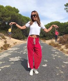 a woman standing in the middle of a road with her hands out and two people behind her