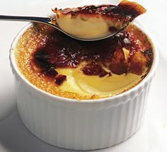 a spoon with some food in it on a white plate and the bowl is filled with pudding