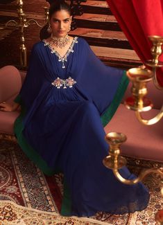 Make a statement at your next Sangeet or cocktail party in this stunning Electric Blue Chiffon Kaftan. With its exquisite embroidery along the neckline and sleeves, this Indo-Western draped kaftan offers the perfect blend of comfort and style for wedding guests. The flowing chiffon fabric drapes beautifully, creating a luxurious silhouette that's ideal for festive occasions. Whether it's a Sangeet or a cocktail event, this kaftan ensures you exude elegance. Composition : Kaftan - Chiffon & Lining - Satin Care: Dry Clean Only and Vacuum Storage This product can be customized for sleeves, blouse length and neckline Delivery : 2-4 weeks as the product is hand crafted. Check Size Guide or choose MySize for free customisation (All Sizes above XL can be made at 15% additional cost) For more info Hand Embellished Georgette Dress For Eid, Eid Hand-embellished Georgette Dress, Party Dresses With Zari Work And Cape Sleeves, Diwali Party Dress With Cape Sleeves, Traditional Evening Gown For Diwali, Party Dresses With Cape Sleeves For Diwali, Traditional Hand Embellished Georgette Dresses, Maxi Length Kaftan For Wedding And Navratri, Wedding Kaftan For Navratri In Maxi Length