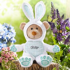 a teddy bear sitting on top of a tree stump with flowers in the back ground