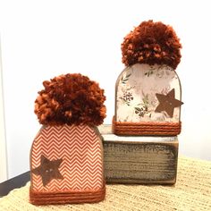 two hats with pom poms sitting on top of a wooden box next to each other