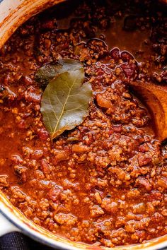 a wooden spoon is in a pot filled with chili and meat sauce, topped with a leaf