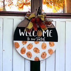 a welcome sign hanging on the side of a white door with pumpkins painted on it