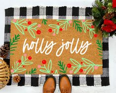 a door mat with the words holly joy written on it next to some pine cones and other holiday decorations