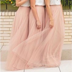 two women standing next to each other wearing pink skirts and white tops with flowers in the background