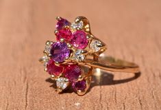 The Hempstead Bubblegum Ruby & Diamond Cocktail Ring. The ring features a reddish purple sapphire center stone with vivid red natural rubies and pink sapphires cascading from the center. Mixed between are diamonds throughout. The ring contains approximately 2 carats total weight by measurement of rubies and sapphires. The total estimated diamond weight by measurement is 0.36 carats. The ring is crafted in 14 karat yellow gold and is currently a finger size 6 yet can be adjusted to any finger Reddish Purple, Filigree Engagement Ring, Diamond Cocktail Ring, Antique Diamond Rings, Purple Sapphire, Diamond Cocktail Rings, Filigree Ring, Antique Diamond, Ruby Diamond