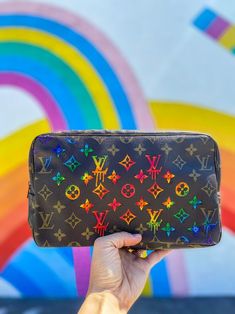 a hand holding up a black louis vuitton bag in front of a rainbow painted wall