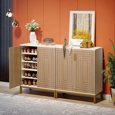 a cabinet with shoes on it in front of an orange wall and potted plant