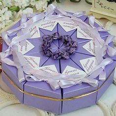 a purple gift box with white tags and ribbons on the lid, sitting on a table next to flowers