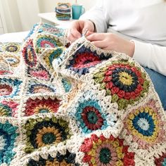 a woman sitting on top of a bed next to a crocheted granny blanket