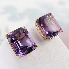 "Natural sparkling purple amethyst gems are basket-set in this vintage pair of 14k yellow gold stud earrings. Each 6 carat faceted rectangular amethyst measures approx. 12mm x 10mm x 7.5mm. The stones are of lovely semi-translucent medium purple color with a slight reddish hue. Together they have a 12 carat total weight in amethyst. The airy sturdy setting shows of the genuine stones nicely. The earring settings and push-on backs are all marked, \"14k\" (gold) and there is an unknown maker's mark on the back of the settings. Overall, this pair is in very good vintage condition with minor pre-owned wear and a slight irregularity to straightness of one post. Please see all photos and below for detailed measurements. This pair would bring a nice pop of color to your ears! Total Wt: 4.4 grams Classic Square Cut Purple Jewelry, Classic Purple Square Cut Jewelry, Classic Purple Jewelry With Rectangular Stone, Purple Rectangular Jewelry With Prong Setting, Purple Rectangular Jewelry For Formal Occasions, Formal Rectangular Purple Jewelry, Formal Purple Rectangular Jewelry, Yellow Gold Stud Earrings, Amethyst Gem