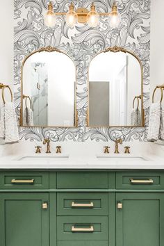 a bathroom vanity with two mirrors and green cabinetry in front of a wallpapered wall