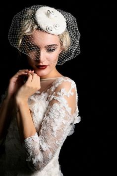 a woman wearing a veil with flowers on her head and holding her hand near her face