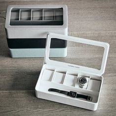 an open watch box on a wooden table with a watch in the middle and two watches inside