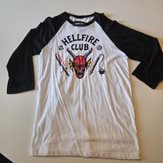 Nwt Strangerthings Hellfire Shirt From Hot Topic. White Grunge Shirt With Screen Print, Edgy White Tops With Logo Print, White Band Merch Shirt With Graphic Design, White Graphic Band Merch Shirt, White Cotton Band Merch Shirt, White Graphic Design Band Merch Shirt, White Cotton Shirt For Fan Merchandise, Urban Style White Long Sleeve Shirt, White Grunge Fan Merchandise Tops