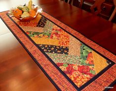 a table runner with pumpkins, apples and squash in it on top of a wooden floor