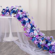 a white table topped with a purple and blue flower arch