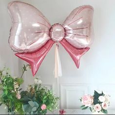 a pink bow balloon sitting on top of a table next to flowers and vases