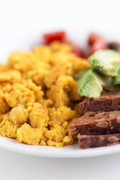 a white plate topped with meat and veggies on top of a bed of scrambled eggs