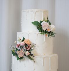 a three tiered white cake with flowers on top and greenery around the edges