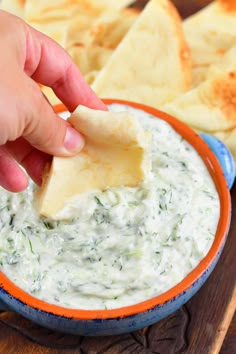 a hand dipping some chips into a bowl of dip