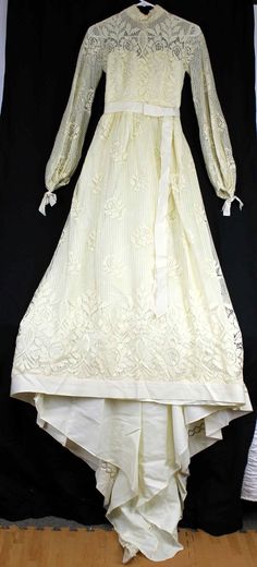 an old white dress is displayed on a black background with wood flooring in the foreground