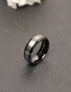 a black and silver ring with the word trust engraved on it, sitting next to a white flower