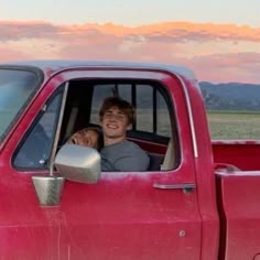 two people are sitting in the back of a red pick - up truck and smiling