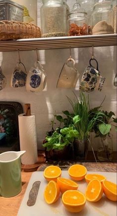 there are oranges on the cutting board next to cups and utensils in this kitchen