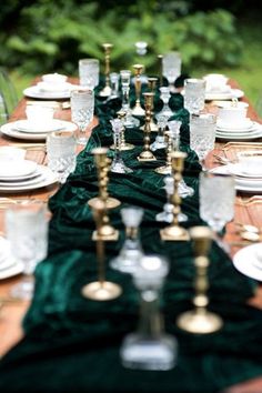 a long table is set with white plates and gold candlesticks, green velvet