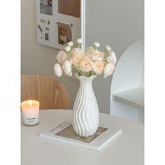 a white vase filled with flowers sitting on top of a table next to a candle