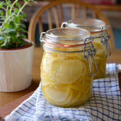 two jars filled with lemon slices sitting on top of a table next to a potted plant