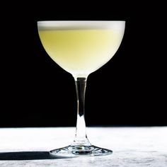 a glass filled with liquid sitting on top of a white counter next to a black background