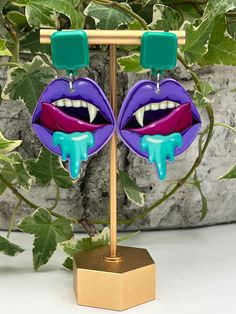 Description: Pastel Goth Vampire Mouth Statement Earrings  These items are individually made with love by me. Details: Handmade item Materials: Acrylic & Resin  Hypo-allergenic stainless steel posts Includes rubber backs Color: Purple & Blue  Length: 2.5" Style: Pastel Goth/ Vampire / Whimsigoth / Cute Emo / Witchy / Kawaii Goth  CARE INSTRUCTIONS: Store out of direct sunlight and keep away from water. it is not recommended to wear these earrings in or around water Handmade Vampire Style Jewelry For Party, Purple Earrings For Halloween Party, Unique Dangle Plug Earrings For Party, Halloween Punk Style Single Earring, Punk Style Single Earring For Halloween, Green Halloween Party Jewelry, Novelty Purple Jewelry For Party, Novelty Purple Party Jewelry, Gothic Earrings For Costume Party