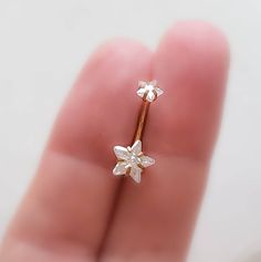 a tiny gold ring with two small white flowers on it's side, in the palm of someone's hand